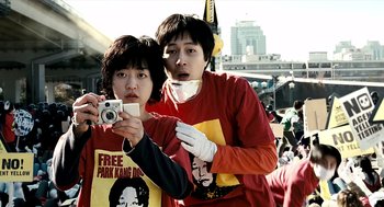 Movie still from “The Host” (2006), directed by Bong Joon Ho – Two young men taking a picture with a camera; Medium shot, Low angle