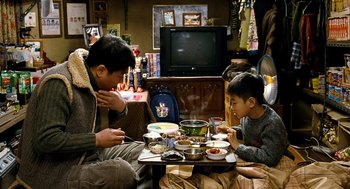 Movie still from “The Host” (2006), directed by Bong Joon Ho – A man and a boy sitting at a table eating food; Medium shot, High angle