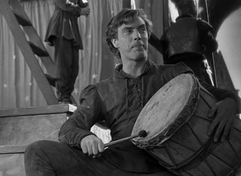 Movie still from “The Hunchback of Notre Dame” (1939), directed by William Dieterle – A man sitting on top of a chair holding a drum; Medium shot, Low angle