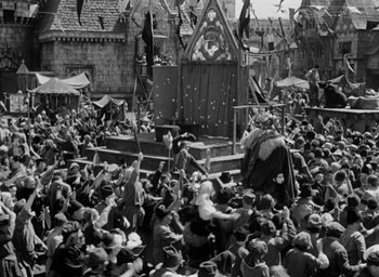 Movie still from “The Hunchback of Notre Dame” (1939), directed by William Dieterle – A crowd of people are gathered around a stage in the middle of a town; Extreme Wide shot, High angle