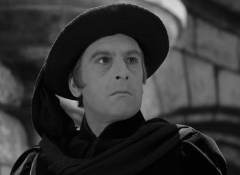 Movie still from “The Hunchback of Notre Dame” (1939), directed by William Dieterle – A black and white photo of a man wearing a hat; Close Up shot, Over the shoulder angle