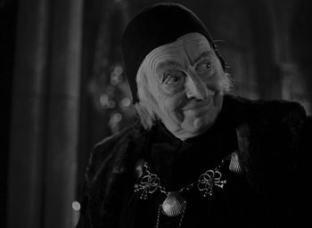 Movie still from “The Hunchback of Notre Dame” (1939), directed by William Dieterle – An old woman wearing a black hat and a black coat; Close Up shot, Over the shoulder angle