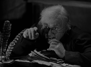 Movie still from “The Hunchback of Notre Dame” (1939), directed by William Dieterle – An old man with glasses is sitting at a table; Close Up shot, High angle