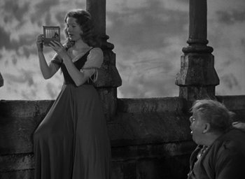 Movie still from “The Hunchback of Notre Dame” (1939), directed by William Dieterle – A woman in a long dress taking a picture of a man; Medium shot, Low angle