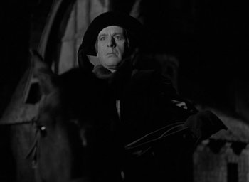 Movie still from “The Hunchback of Notre Dame” (1939), directed by William Dieterle – A black and white photo of a man in a hooded cloak; Medium shot, Low angle