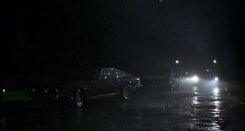 Movie still from “The Ice Storm” (1997), directed by Ang Lee – A couple of cars parked on top of a wet road at night; Extreme Wide shot, High angle