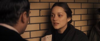 Movie still from “The Immigrant” (2013), directed by James Gray – A woman sitting against a brick wall holding a piece of paper; Close Up shot, Over the shoulder angle