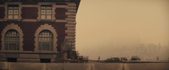 Movie still from “The Immigrant” (2013), directed by James Gray – A brick building with a person standing in the background; Extreme Wide shot, Low angle