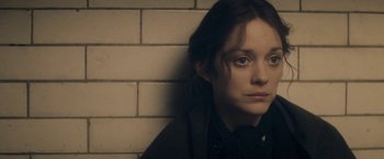 Movie still from “The Immigrant” (2013), directed by James Gray – A woman sitting against a brick wall looking at the camera; Close Up shot, High angle
