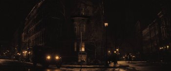 Movie still from “The Immigrant” (2013), directed by James Gray – A street scene of a building at night with street lights; Extreme Wide shot, High angle