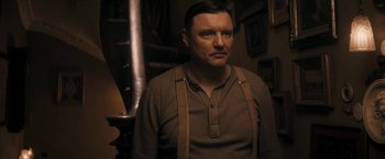 Movie still from “The Immigrant” (2013), directed by James Gray – A man in a brown shirt and suspenders looks at the camera; Medium shot, Low angle