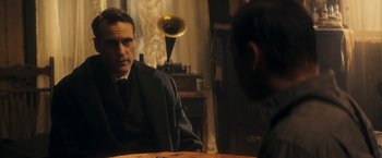 Movie still from “The Immigrant” (2013), directed by James Gray – A man sitting at a table in front of an old gramaphone; Medium shot, Over the shoulder angle