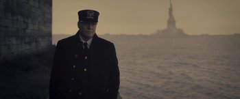 Movie still from “The Immigrant” (2013), directed by James Gray – A man in a uniform standing in front of a body of water; Medium shot, Low angle