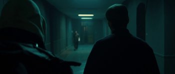 Movie still from “The Imposter” (2012), directed by Bart Layton – A man standing in a dark hallway with a person walking by; Wide shot, Over the shoulder angle