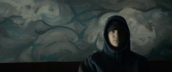Movie still from “The Imposter” (2012), directed by Bart Layton – A man wearing a hooded sweatshirt in front of a painting; Close Up shot, Low angle