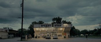 Movie still from “The Imposter” (2012), directed by Bart Layton – Two cars are parked in front of a gas station; Extreme Wide shot, Low angle