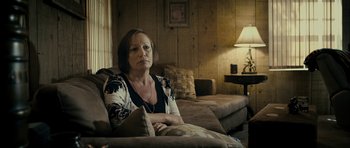 Movie still from “The Imposter” (2012), directed by Bart Layton – A woman sitting on a couch in a living room; Medium shot, Over the shoulder angle