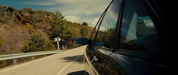 Movie still from “The Imposter” (2012), directed by Bart Layton – A car driving down a road with trees in the background; Wide shot, Low angle