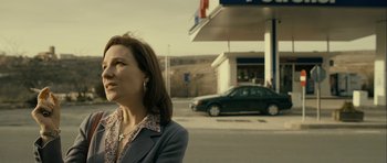 Movie still from “The Imposter” (2012), directed by Bart Layton – A woman standing in front of a gas station next to a car; Medium shot, Over the shoulder angle