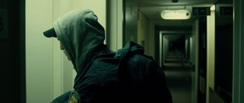 Movie still from “The Imposter” (2012), directed by Bart Layton – A person in a hooded jacket in a dark hallway; Medium shot, Over the shoulder angle