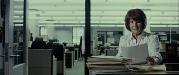Movie still from “The Imposter” (2012), directed by Bart Layton – A man in a white shirt is holding a stack of papers in an office; Medium shot, Over the shoulder angle