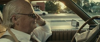 Movie still from “The Imposter” (2012), directed by Bart Layton – An older man sitting in the back seat of a car; Close Up shot, Over the shoulder angle