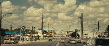 Movie still from “The Imposter” (2012), directed by Bart Layton – Cars driving down a street under a cloudy sky; Extreme Wide shot, Low angle