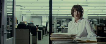 Movie still from “The Imposter” (2012), directed by Bart Layton – A woman sitting at a desk in an office with a stack of papers in front of her; Medium shot, Over the shoulder angle