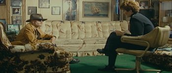 Movie still from “The Imposter” (2012), directed by Bart Layton – Two people sitting on a couch in a living room; Wide shot, High angle