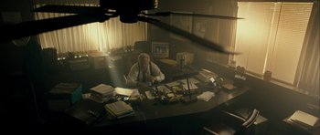 Movie still from “The Imposter” (2012), directed by Bart Layton – A man sitting at a desk in an office setting; Wide shot, High angle