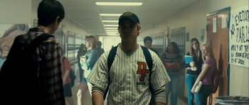 Movie still from “The Imposter” (2012), directed by Bart Layton – A man in a baseball uniform standing in a school hallway; Medium shot, Over the shoulder angle