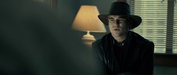 Movie still from “The Imposter” (2012), directed by Bart Layton – A man wearing a hat sitting in front of a table lamp; Close Up shot, Over the shoulder angle