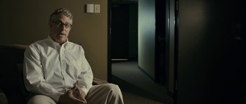 Movie still from “The Imposter” (2012), directed by Bart Layton – An older man sitting on a chair in a room; Medium shot, Over the shoulder angle