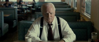 Movie still from “The Imposter” (2012), directed by Bart Layton – An older man sitting in front of a table; Close Up shot, Over the shoulder angle