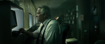 Movie still from “The Imposter” (2012), directed by Bart Layton – An older man sitting at a computer in a dark room; Medium shot, Low angle