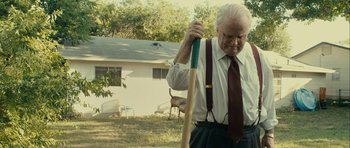 Movie still from “The Imposter” (2012), directed by Bart Layton – An older man holding a baseball bat in a yard; Medium shot, Low angle