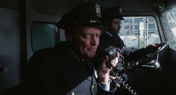 Movie still from “The In-Laws” (1979), directed by Arthur Hiller – Two police officers in uniform talking on a phone; Medium shot, Over the shoulder angle