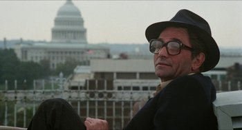 Movie still from “The In-Laws” (1979), directed by Arthur Hiller – A man wearing a hat and glasses in front of the us capitol building; Close Up shot, Low angle