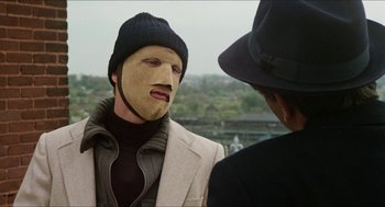 Movie still from “The In-Laws” (1979), directed by Arthur Hiller – A man with a mask on talking to another man wearing a hat; Close Up shot, Over the shoulder angle