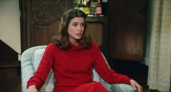 Movie still from “The In-Laws” (1979), directed by Arthur Hiller – A woman sitting on a chair wearing a red dress; Medium shot, Over the shoulder angle