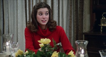Movie still from “The In-Laws” (1979), directed by Arthur Hiller – A woman in a red sweater sitting at a table with yellow flowers; Close Up shot, Over the shoulder angle