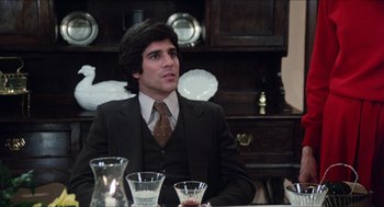 Movie still from “The In-Laws” (1979), directed by Arthur Hiller – A man sitting at a dinner table in front of two glasses of water; Medium shot, Over the shoulder angle