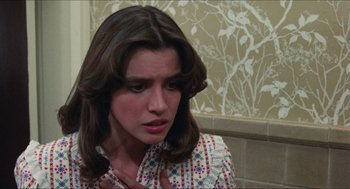Movie still from “The In-Laws” (1979), directed by Arthur Hiller – A woman with long brown hair is sitting in a room; Close Up shot, Over the shoulder angle