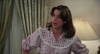 Movie still from “The In-Laws” (1979), directed by Arthur Hiller – A woman in a floral shirt is standing in front of a bed; Medium shot, Over the shoulder angle