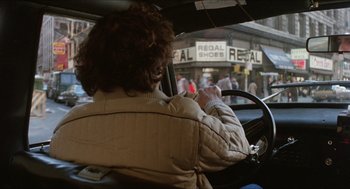 Movie still from “The In-Laws” (1979), directed by Arthur Hiller – A woman sitting in the driver's seat of a car driving down a street; Wide shot, Over the shoulder angle