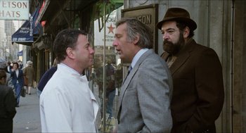 Movie still from “The In-Laws” (1979), directed by Arthur Hiller – A group of men standing next to each other on the street; Medium shot, Over the shoulder angle