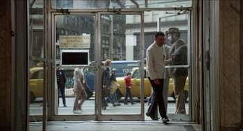 Movie still from “The In-Laws” (1979), directed by Arthur Hiller – A group of people walking on the sidewalk; Wide shot, Over the shoulder angle