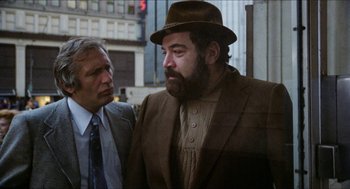 Movie still from “The In-Laws” (1979), directed by Arthur Hiller – A man in a suit and a hat standing next to another man in a suit; Medium shot, Over the shoulder angle