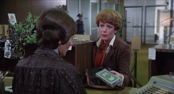 Movie still from “The In-Laws” (1979), directed by Arthur Hiller – Two women are sitting at a table and one of the women is holding a book; Medium shot, Over the shoulder angle