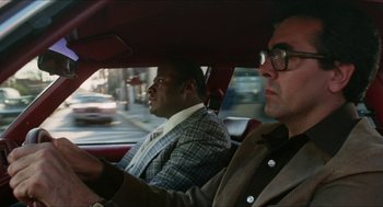 Movie still from “The In-Laws” (1979), directed by Arthur Hiller – Two men in suits driving in a red car; Medium shot, Over the shoulder angle